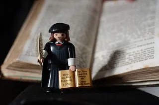Eine Playmobil-Figur von Martin Luther mit Büchern und Schreibfeder.
