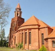 Eine rote Backsteinkirche mit einem hohen Glockenturm unter blauem Himmel.