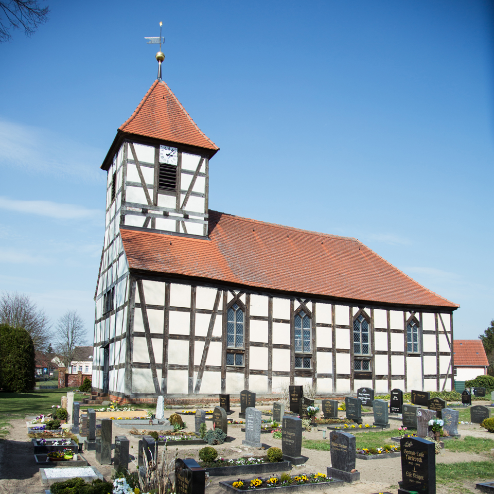  Eine Fachwerkkirche mit Kirchturm, umgeben von einem Friedhof.