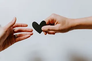 Eine Hand gibt ein Herz, als Symbol für Nächstenliebe und Gemeinschaft.