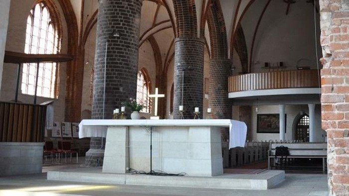 Der Innenraum einer Kirche mit Altar, Bänken und Backsteinsäulen.